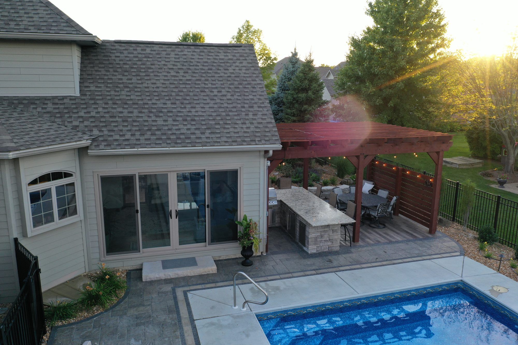 Drone view of a backyard pool, pergola and outdoor kitchen at sunset