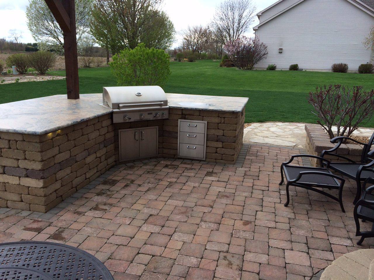 Stone outdoor kitchen with a built-in grill on a brick paver patio
