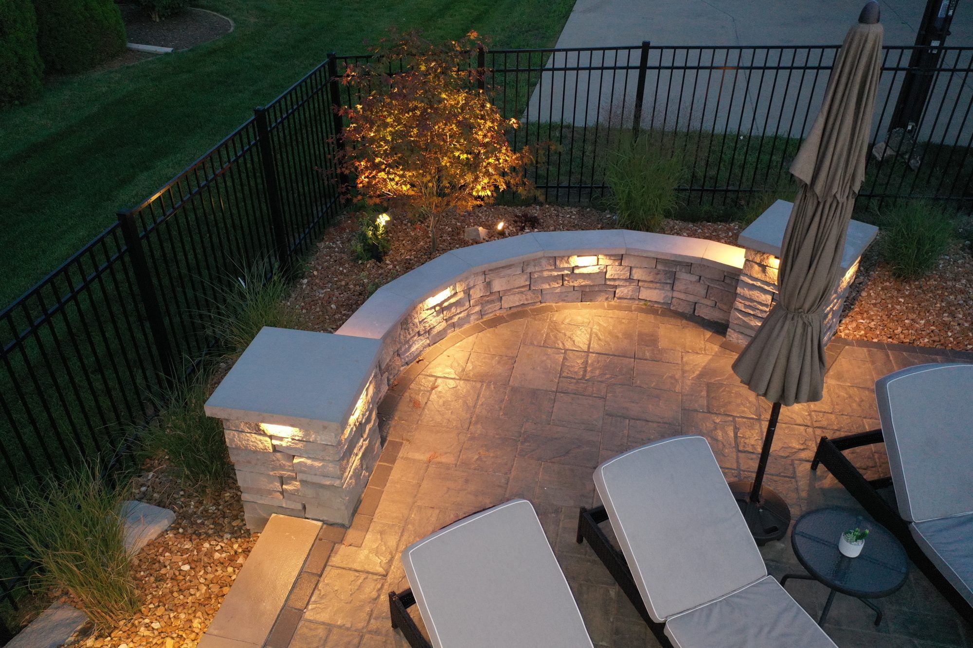 Curved stone seat wall with built-in lights and lounge chairs on a pool deck