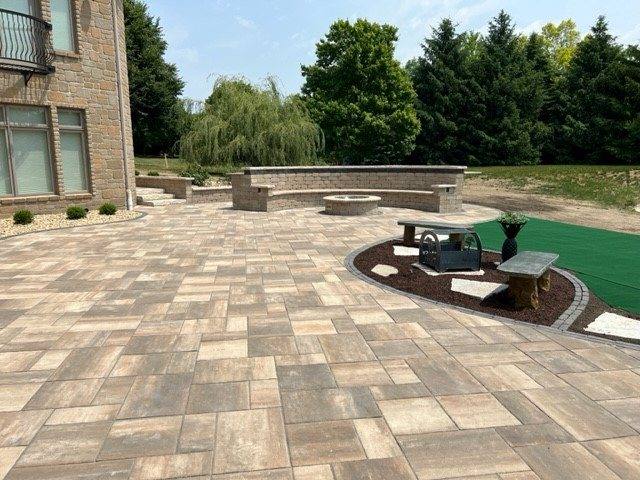 Large backyard paver patio with a built-in fire pit and seat wall