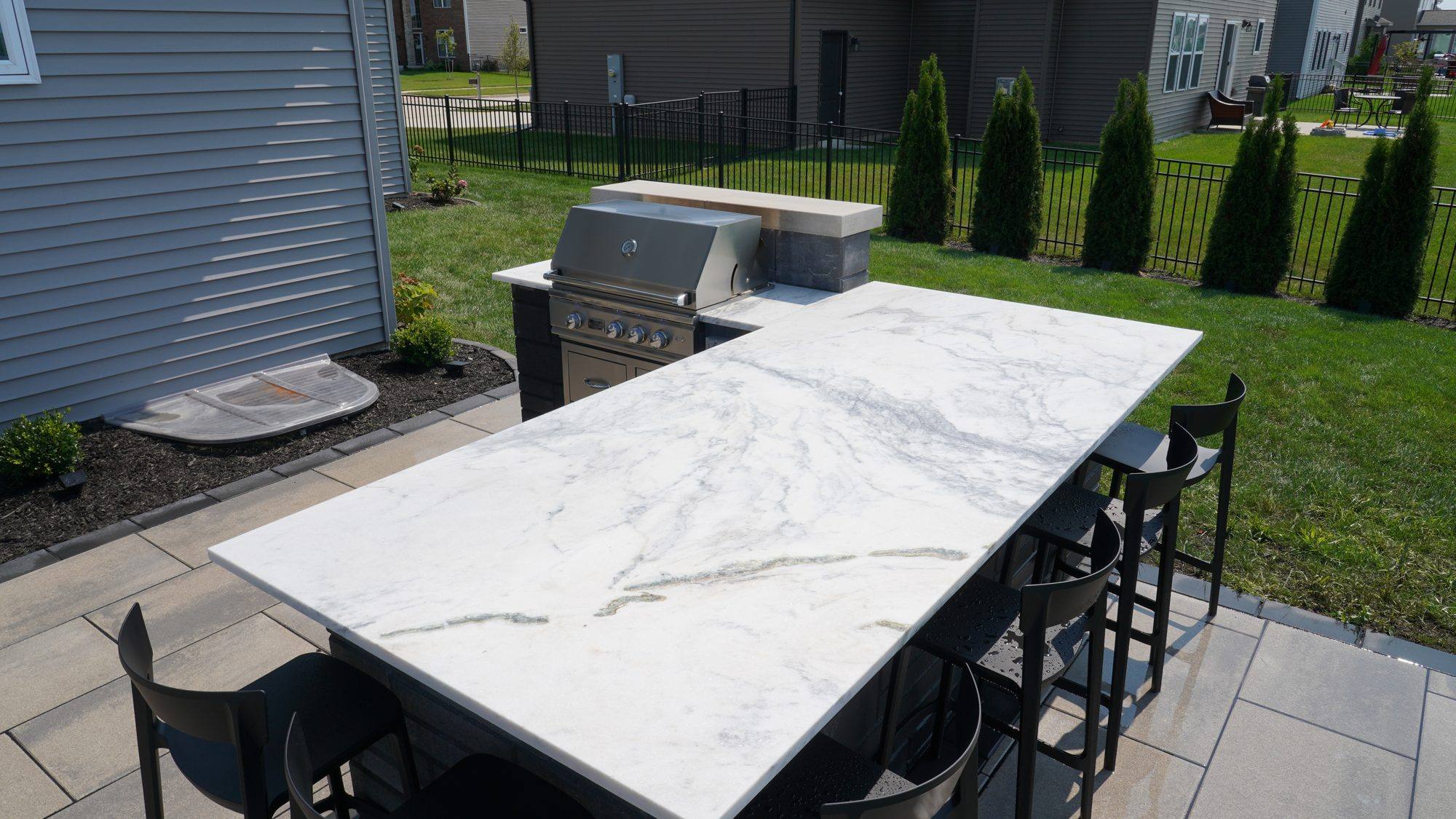 Outdoor kitchen with a long marble-look bar top and seating