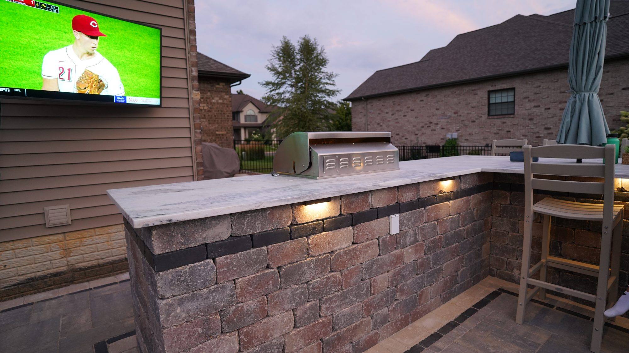 Outdoor kitchen bar with lighting and a mounted TV on a paver patio