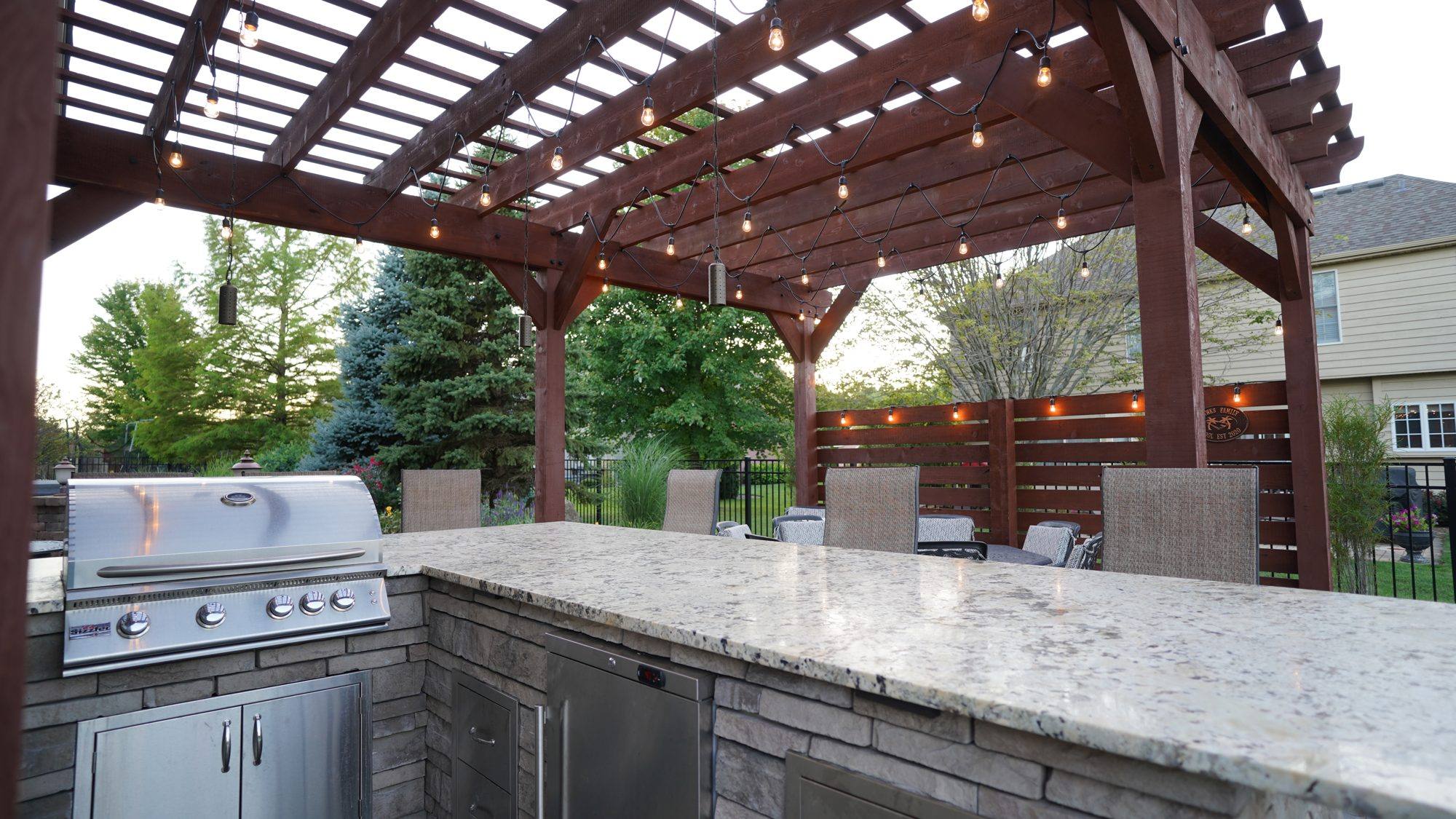 Outdoor kitchen bar with stainless grill and granite counter under a pergola