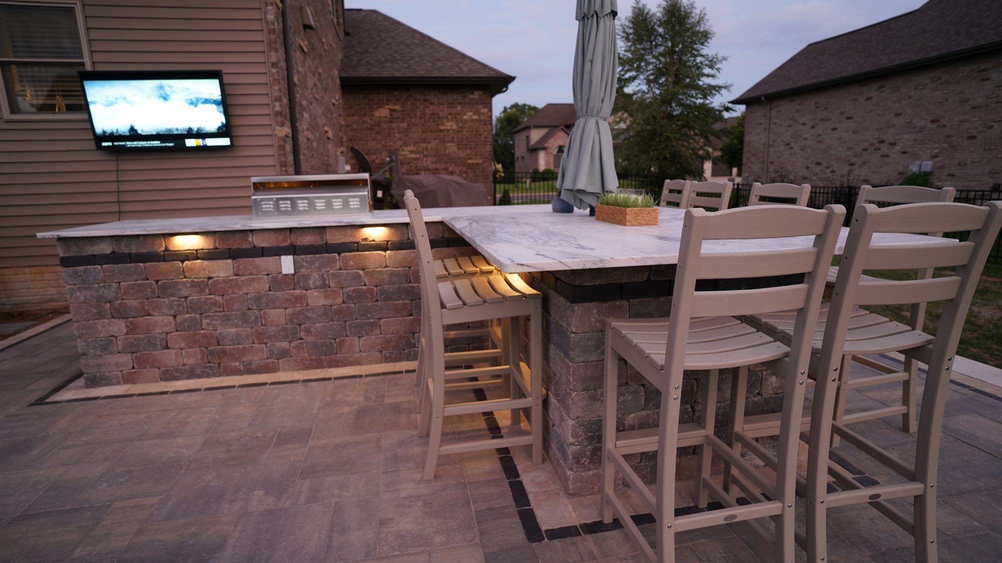 Outdoor kitchen and raised dining bar on a paver patio at dusk