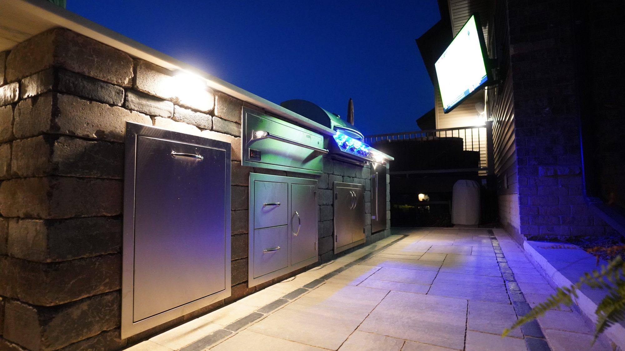 Outdoor kitchen with stainless doors and accent lighting at night