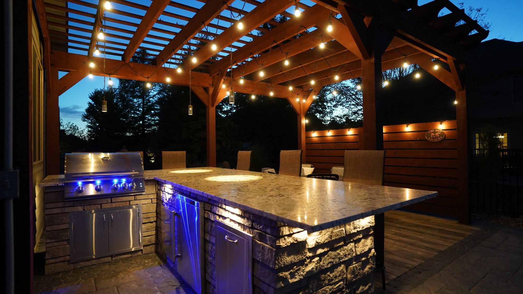 Outdoor kitchen under a pergola lit with string lights at night