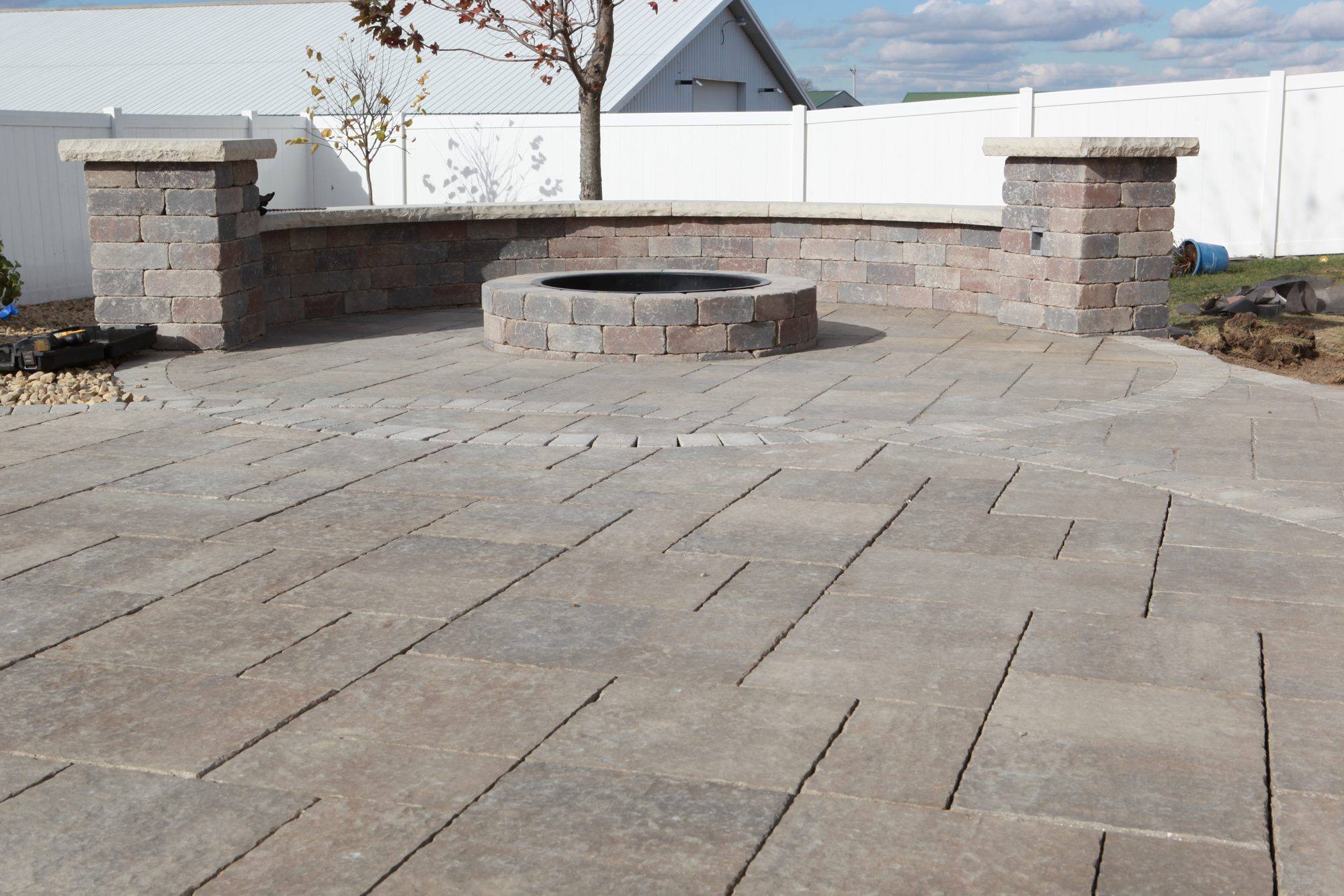 Paver patio with a round fire pit and a seat wall with pillars