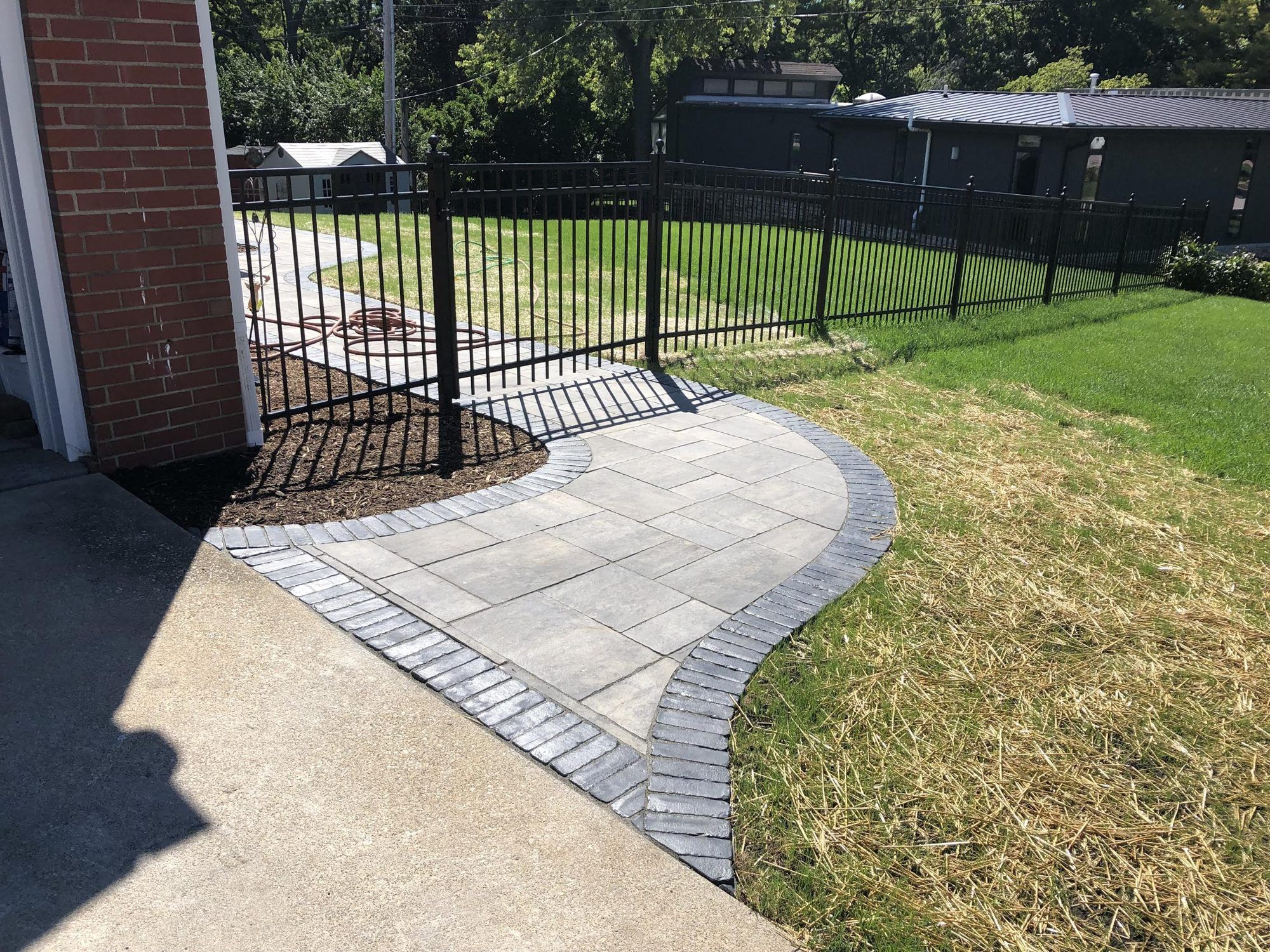 Curved paver walkway with a charcoal border leading to a black aluminum gate