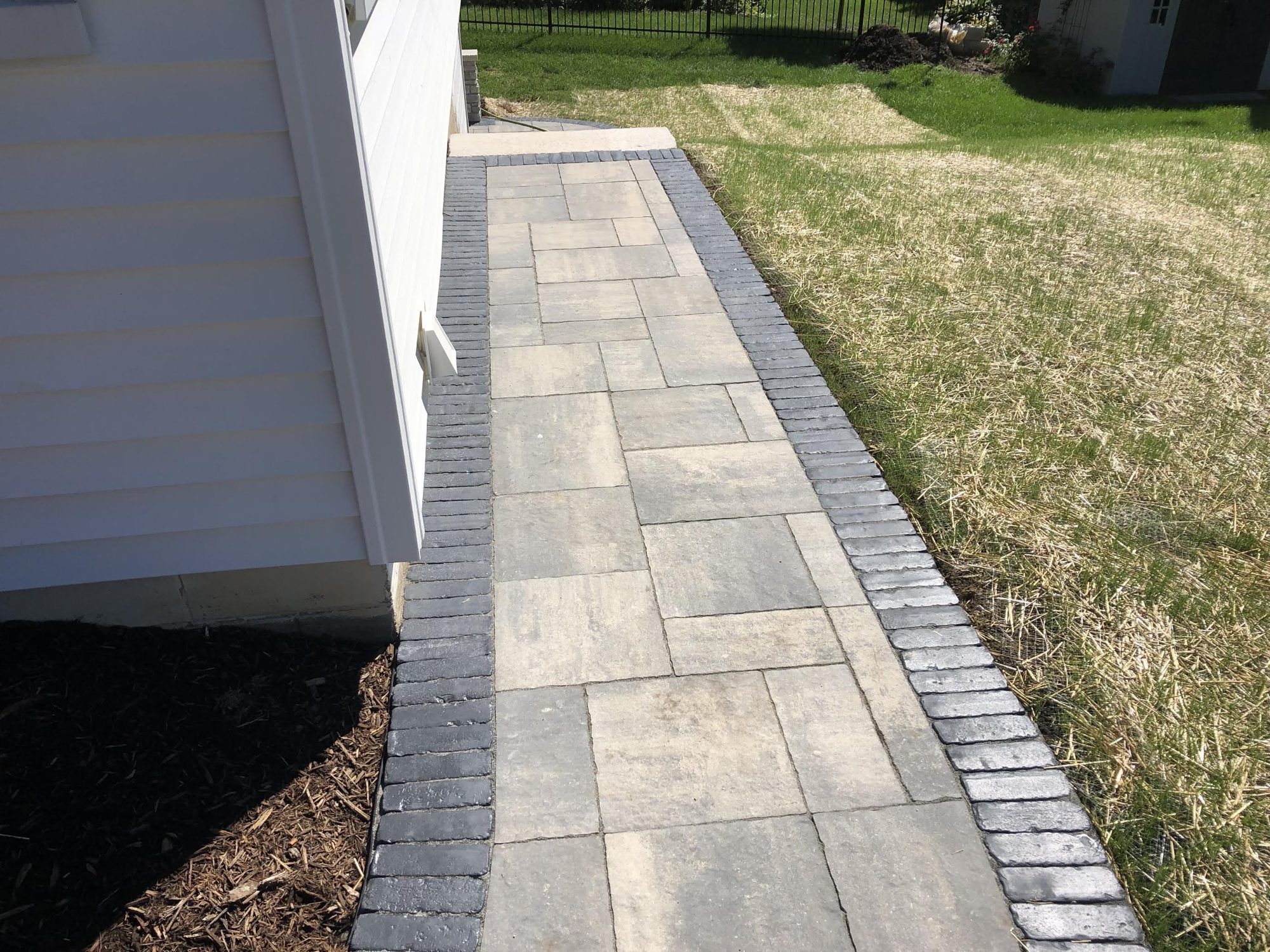 Large-format paver walkway with a dark soldier-course border along the side of a house