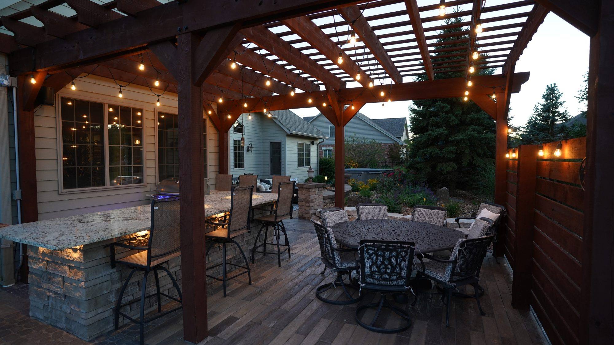 Pergola dining area with string lights, bar seating and an outdoor kitchen