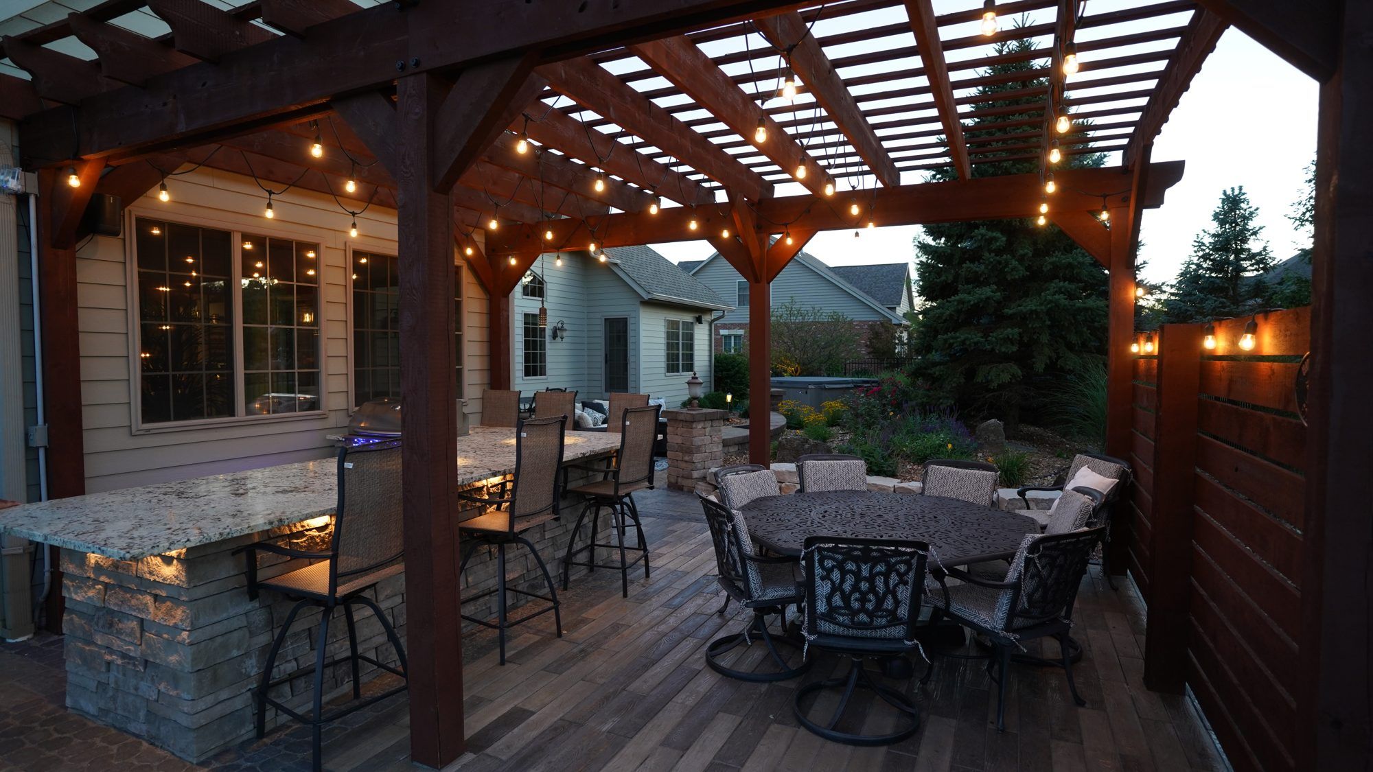 Pergola dining area with string lights, bar seating and an outdoor kitchen
