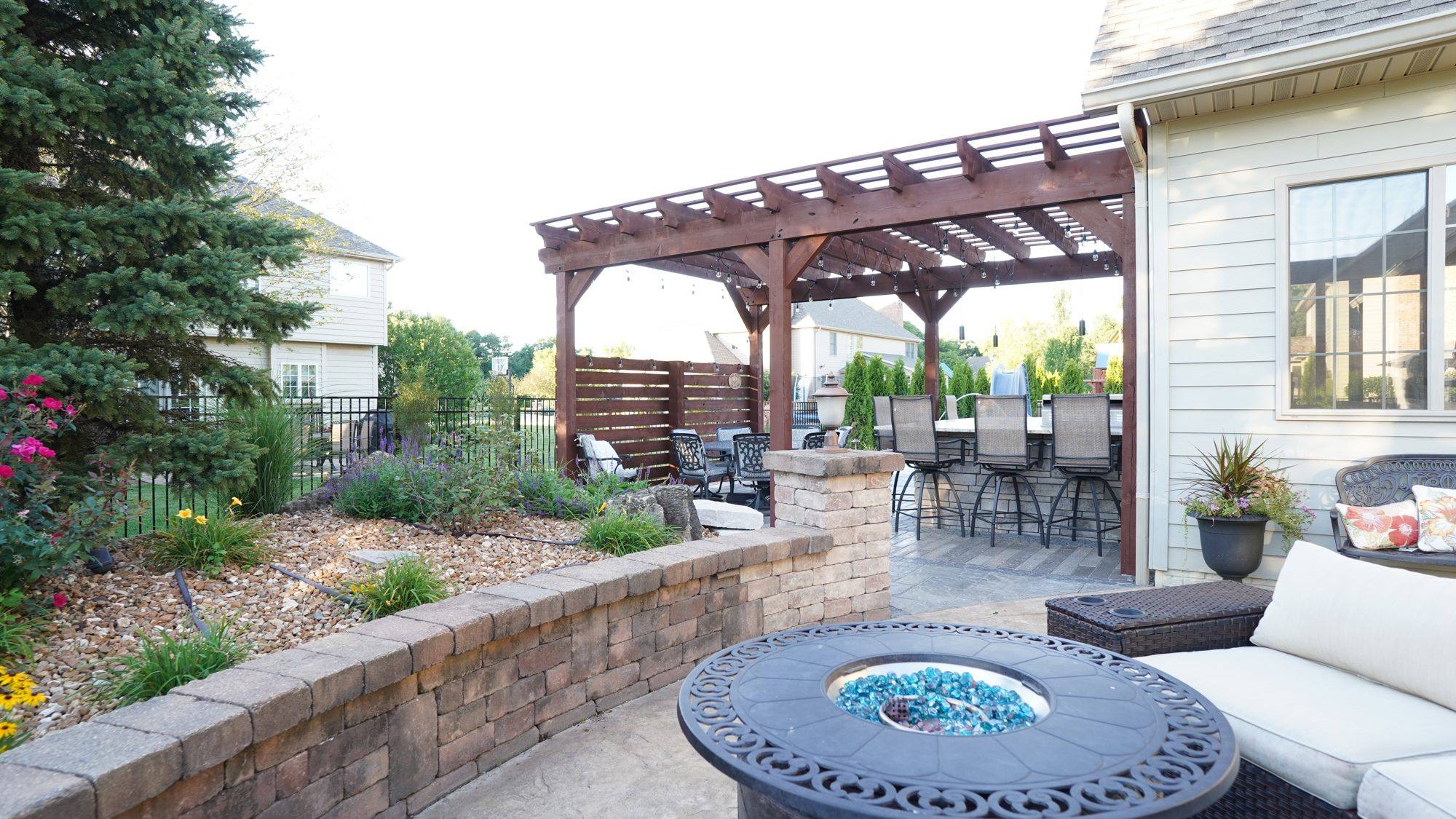 Pergola patio with a fire table, seat wall and landscape beds