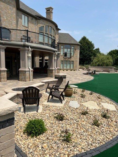 Patio and river-rock landscape bed behind a large stone home