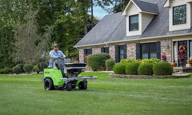 Lawn technician treating a front lawn with a ride-on spreader-sprayer