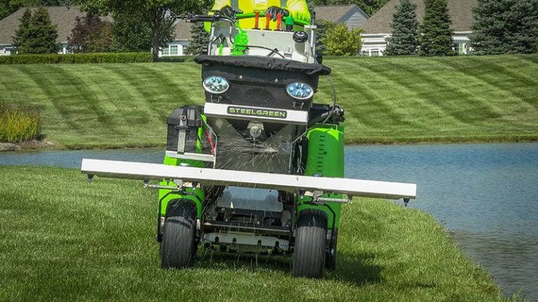 Ride-on spreader-sprayer applying granular fertilizer and a liquid spray to a striped lawn