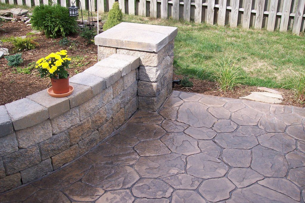 Stamped concrete patio with a stone seat wall, pillar cap and potted mums